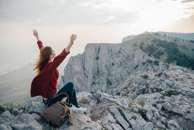 Rear view of woman sitting on rock against sky