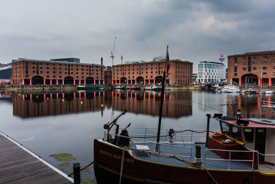 Sailboats moored on river by buildings against sky