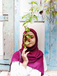 Portrait of woman holding plant against wall