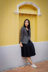 Portrait of young woman standing against wall