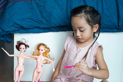 Cute girl playing with doll while sitting on floor