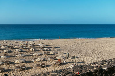 Deck chairs and parasols at beach against clear blue sky