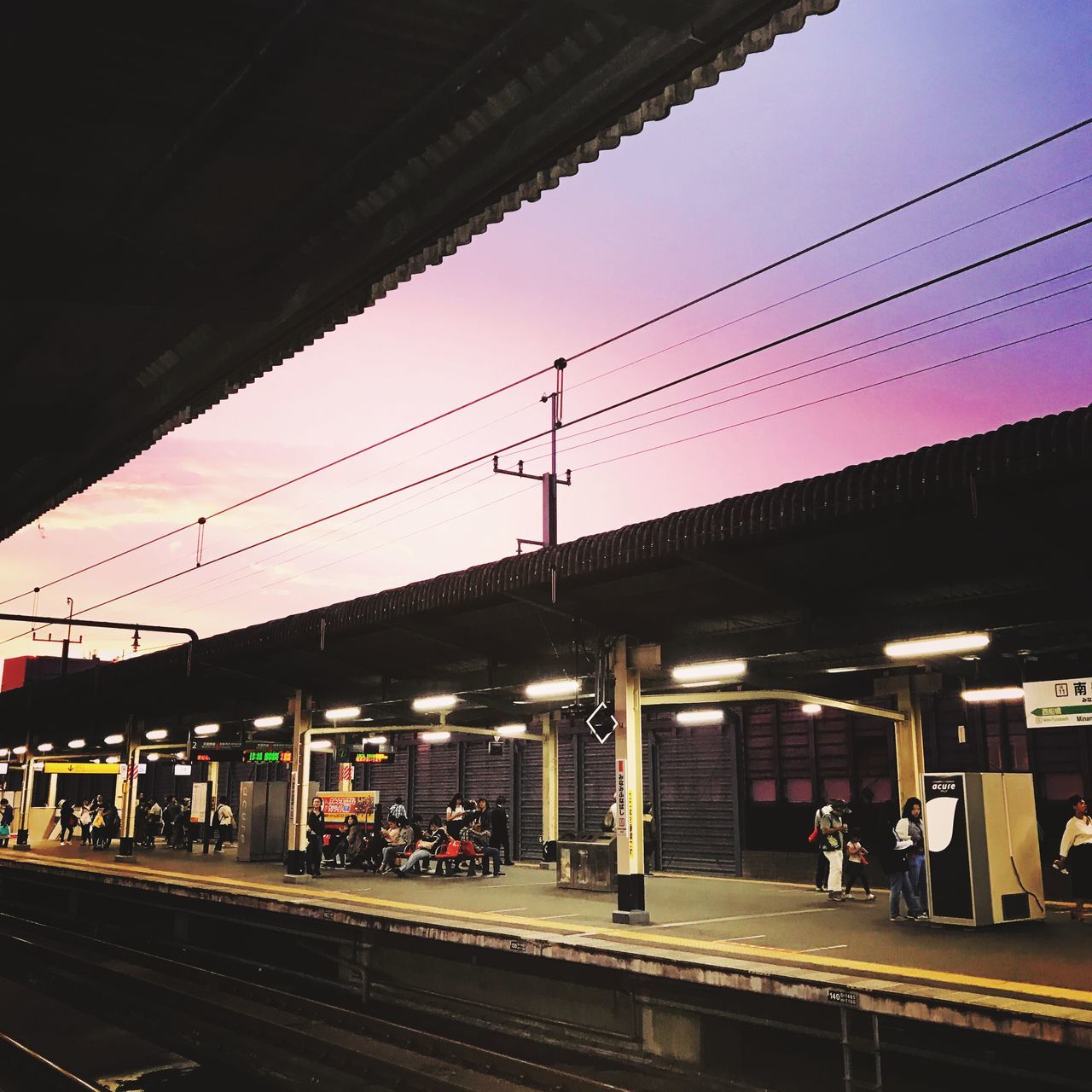 transportation, sky, railroad station platform, rail transportation, railroad station, architecture, built structure, public transportation, group of people, real people, mode of transportation, sunset, track, electricity, railroad track, men, cable, illuminated, power line, train, outdoors, waiting