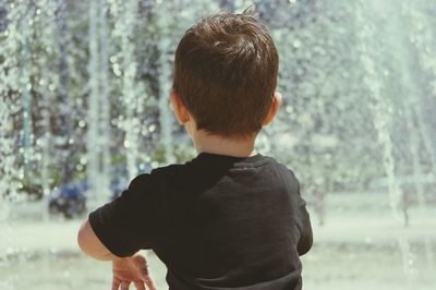 Rear view of boy playing by fountain in city