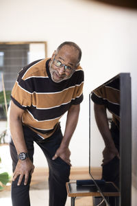 Elderly man looking away while standing by television at home