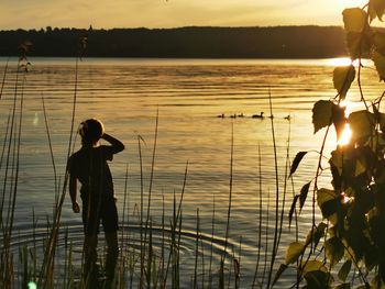 Rear view of girl standing in lake against sky during sunset