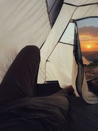 Low section of person relaxing on bed at sunset