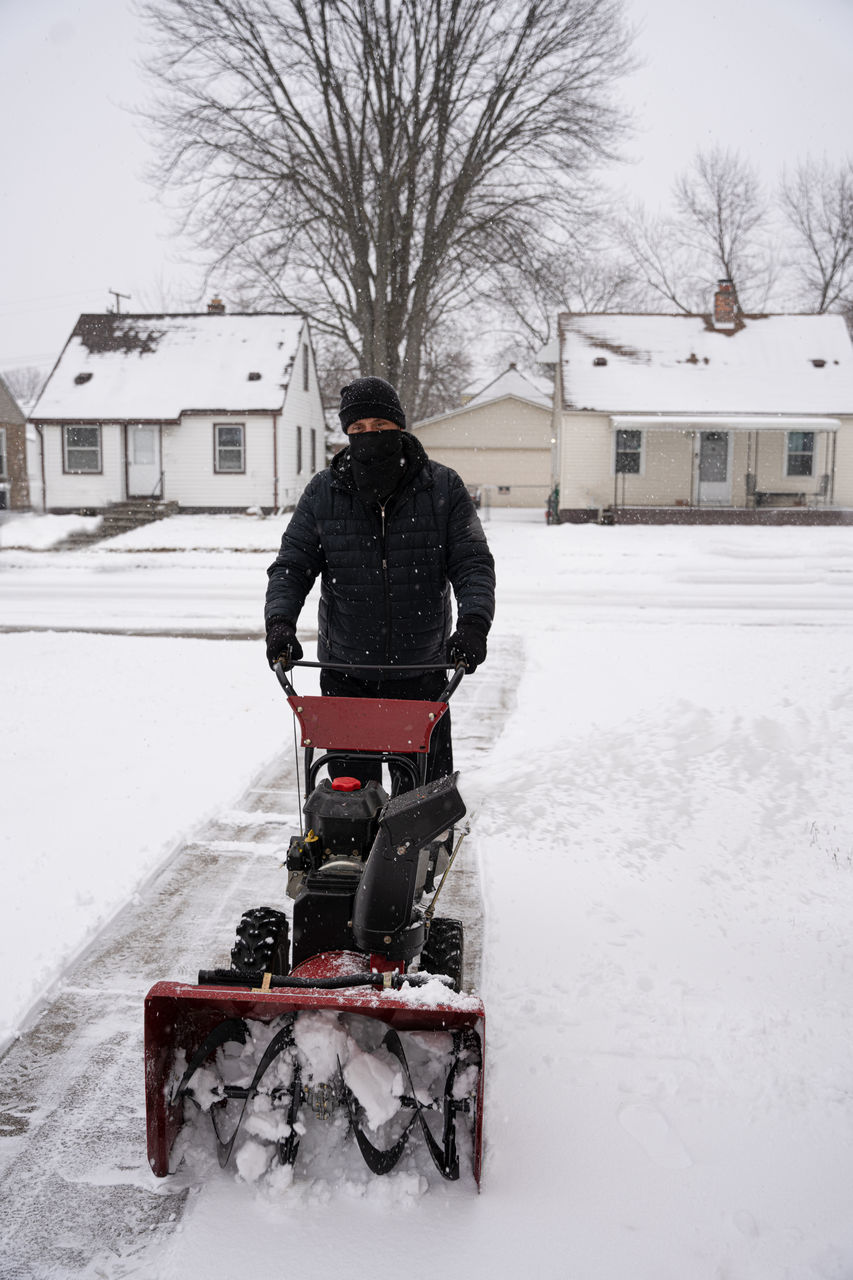 REAR VIEW OF MAN RIDING MOTORCYCLE ON SNOW COVERED FIELD BY HOUSE