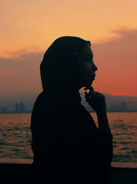 Woman looking at sea against sky during sunset