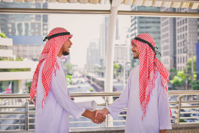 Side view of smiling businessman shaking hands with colleague on elevated road in city