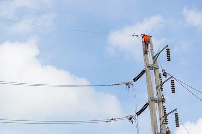 Low angle view of worker working on power line against sky