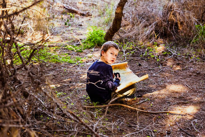 Boy holding paper while sitting in forest