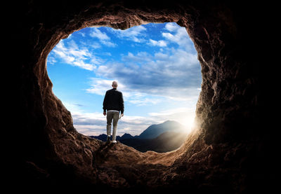 Rear view of man standing in cave against sky