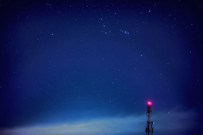 Low angle view of illuminated communication tower against star field