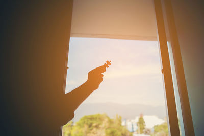 Silhouette hand holding jigsaw piece against sky during sunset