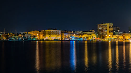 Illuminated buildings by sea against sky at night