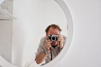 Reflection of man photographing with camera seen in mirror at home