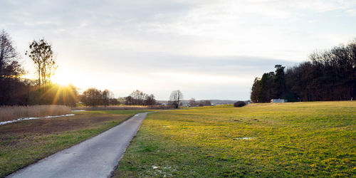 Road amidst field against sky during sunset