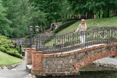 A woman stands on an old bridge in the park in the summer