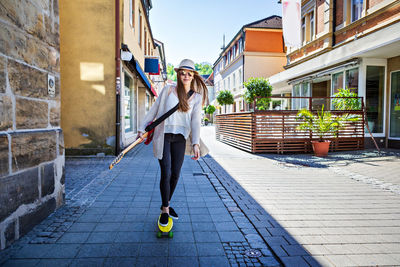 Portrait of young woman with guitar skateboarding on street in city