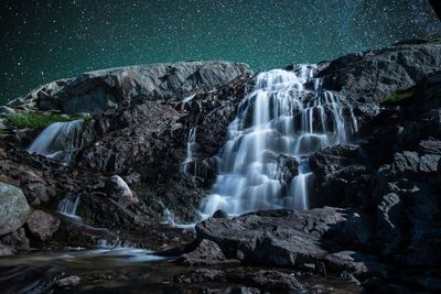 Low angle view of waterfall on rocky mountain against star field sky