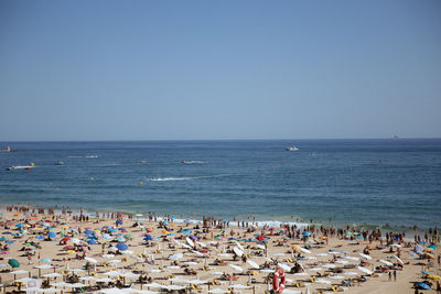 Scenic view of sea against clear sky of people on beach in portugal. 