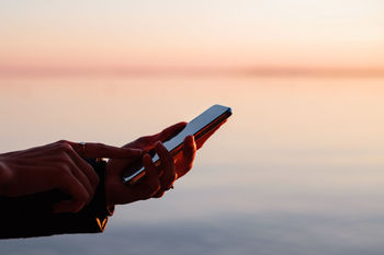 Hands holding smart phone against sky during sunset