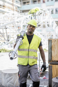 Construction worker looking away while carrying metal rod at site