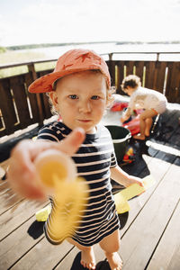 Portrait of cute boy giving toy while standing outdoors during sunny day