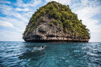 Man on rock by sea against sky