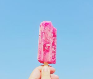 Cropped image of person holding popsicle against blue background