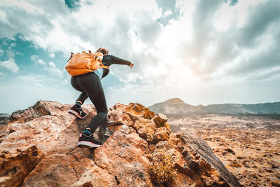 Man standing on rock by mountain against sky