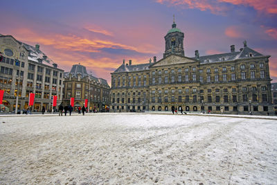 Snowy damsquare with the royal palace in amsterdam at sunset