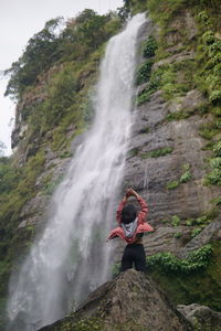 Full length of woman standing on rock against waterfall