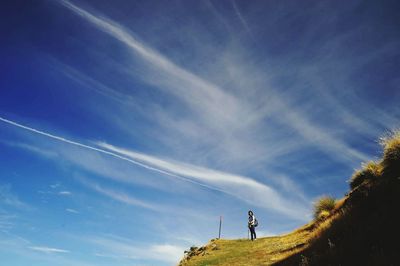 Low angle view of woman standing on mountain against blue sky