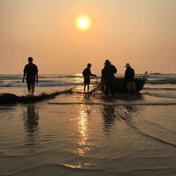 Fishermen with fishing net while standing in sea during sunrise