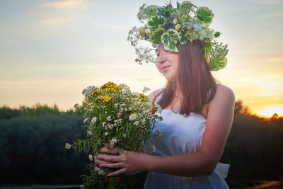 Portrait of young woman standing against sky during sunset