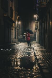 Rear view of man walking on wet street in city during rainy season