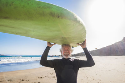 Portrait of smiling man on beach with surfboard against sky