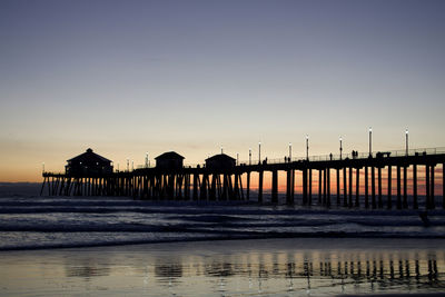 Silhouette pier on beach against clear sky during sunset