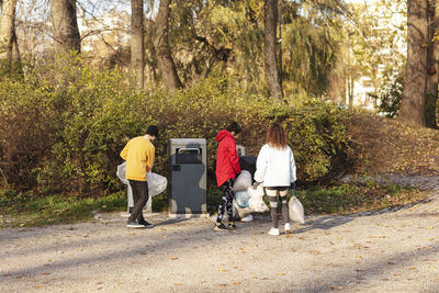 Young male and female environmentalists holding waste by garbage can