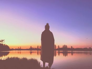 Rear view of silhouette woman standing by lake against sky during sunset