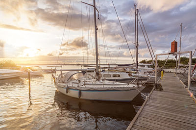 Sailboats moored on sea against sky during sunset