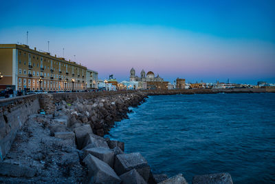 Buildings by sea against blue sky