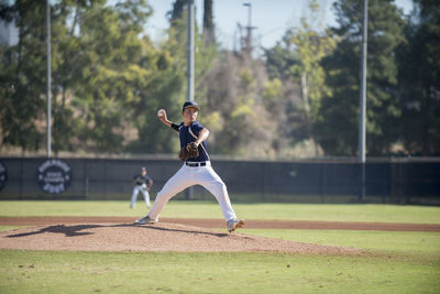 Teen baseball player pitcher in blue uniform in full wind up on the mound