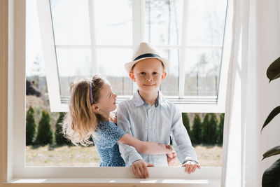 Brother and sister hugging whilst at home looking through a window