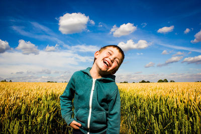 Cheerful boy standing on field against sky