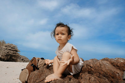 Portrait of cute baby girl gesturing while sitting on rock at beach