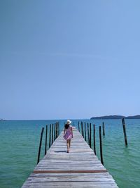 Rear view of man on pier over sea against clear sky