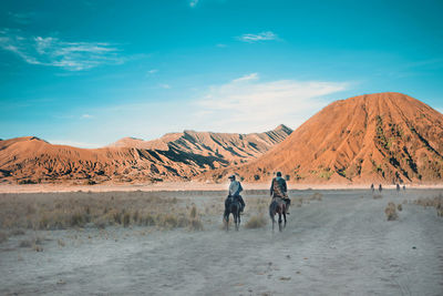 Rear view of men horseback riding at desert against mountains and sky